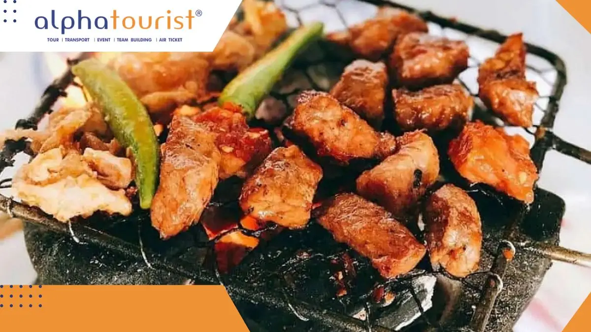 Một đĩa thịt bò thái quân cờ đã được tẩm ướp gia vị màu đỏ au, đặt cạnh một bếp than hồng nhỏ trên bàn ăn tại nhà hàng Lạc Cảnh