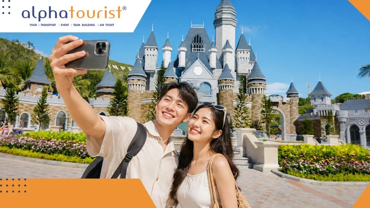 Một cặp đôi trẻ châu Á đang tươi cười rạng rỡ khi chụp ảnh tự sướng bằng điện thoại trước lâu đài nguy nga của VinWonders Nha Trang dưới bầu trời xanh trong